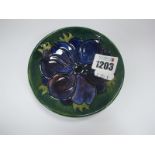 A Moorcroft Pottery Circular Pin Tray, painted in the Clematis pattern on a dark green ground,