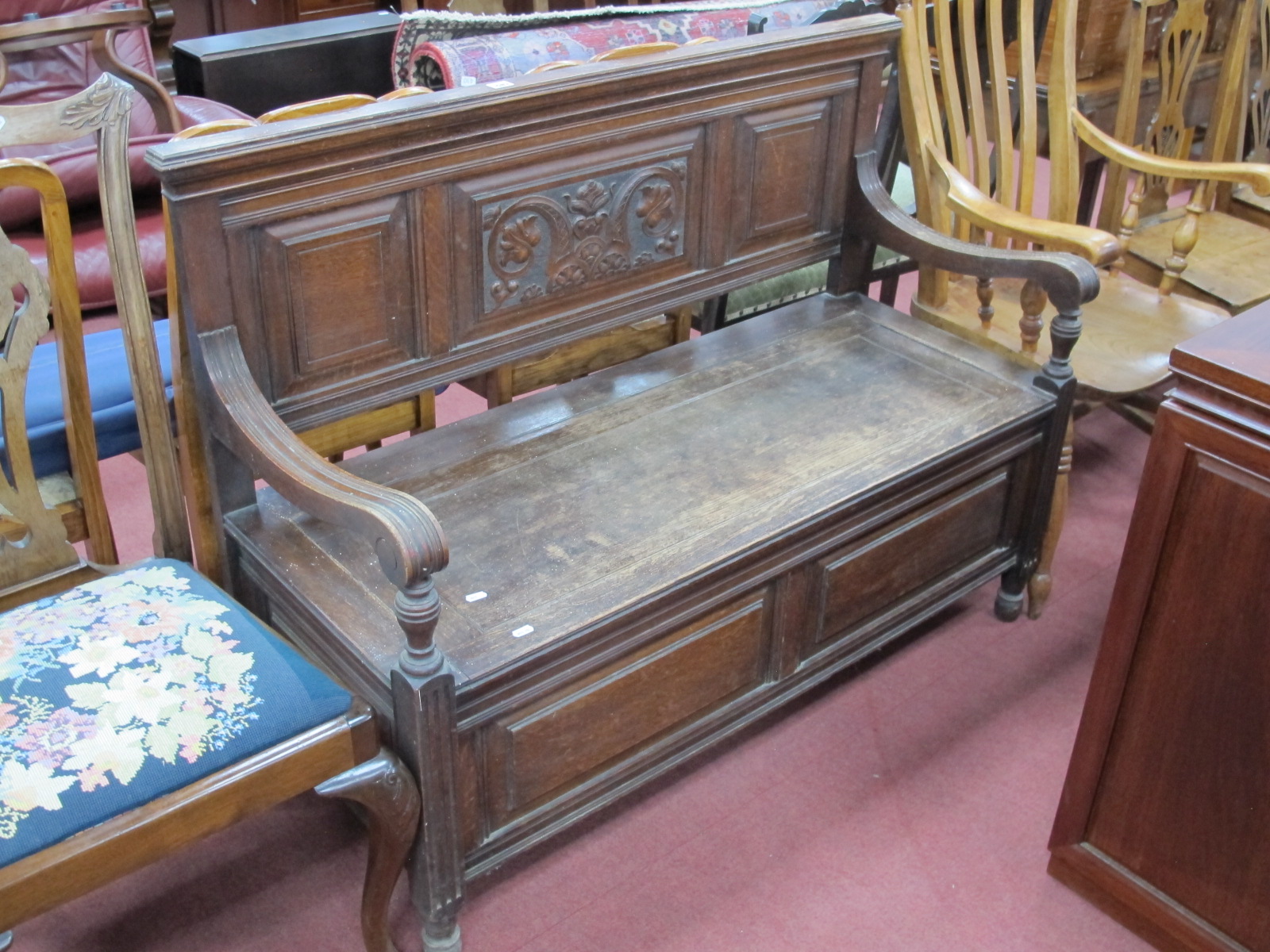 An Early XX Century Oak Hall Bench, with a panelled back, shaped arms, hinged seat, panelled base,