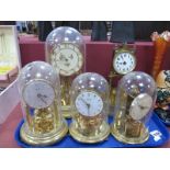 Two Kundo Brass Anniversary Clocks, under glass domes, one other and another under plastic dome