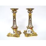 A Pair of Royal Crown Derby Porcelain Candlesticks, the shaped square bases moulded with dolphins,