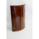 A Georgian mahogany bow front corner cabinet with brass butterfly hinges