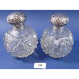 A pair of Victorian cut glass and silver topped large scent bottles with embossed floral