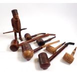 A collection of eight pipes including a carved man concealing a pipe standing 17cm tall