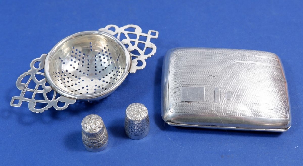 A silver cigarette case 55g, a silver teastrainer, Birmingham 1933, 30g and two silver thimbles, one