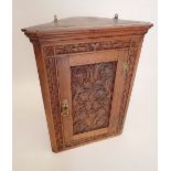 An oak corner cupboard with carved scrollwork decoration to door