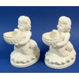 A Victorian pair of porcelain mer children holding shell form salts, 15cm tall