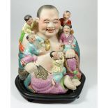 A Chinese polychrome bisque group of seated Buddha and children, on stand, 29cm