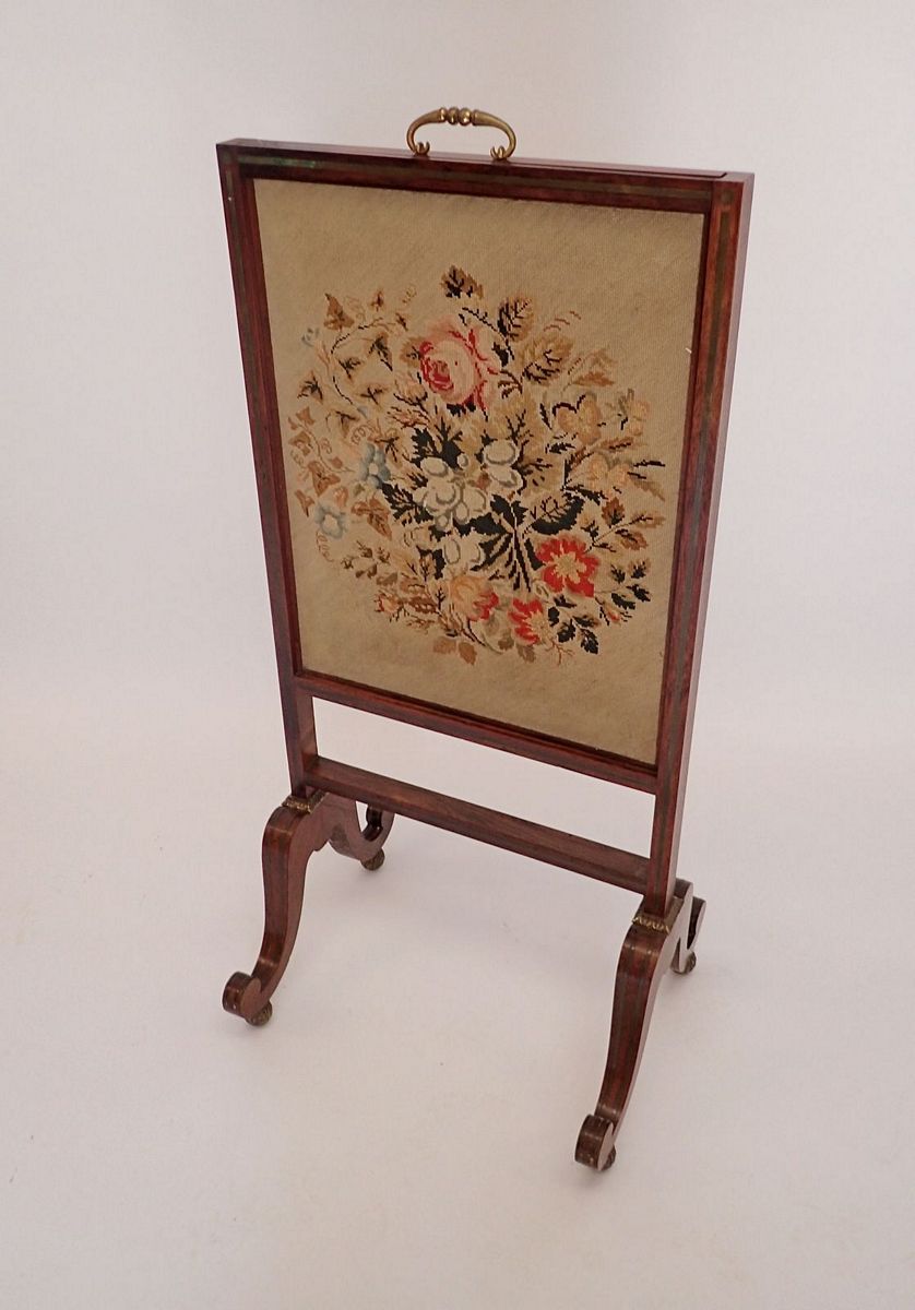 An early 19th century rosewood firescreen with vertical sliding tapestry panel, all on twin scroll