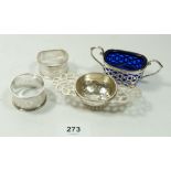 A silver salt with blue glass liner, a silver tea strainer and two silver napkin rings, 96g