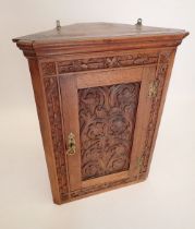 An oak corner cupboard with carved scrollwork decoration to door