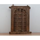 A Middle Eastern/Indian wooden window and frame, three metal bars to the front, decoratively carved,