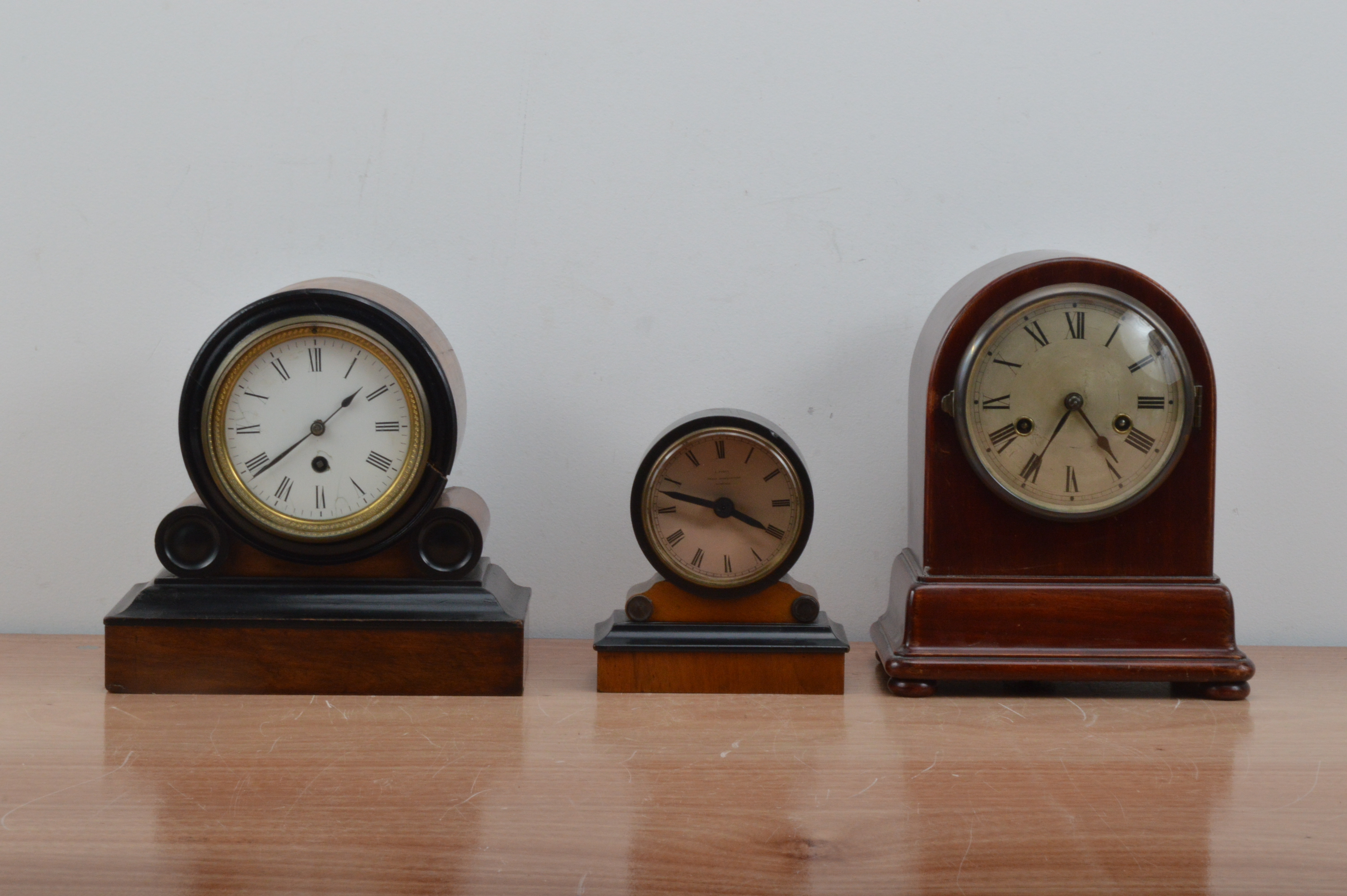 Three domed wooden cased mantle clocks, all dials with Roman numerals, the larger two with