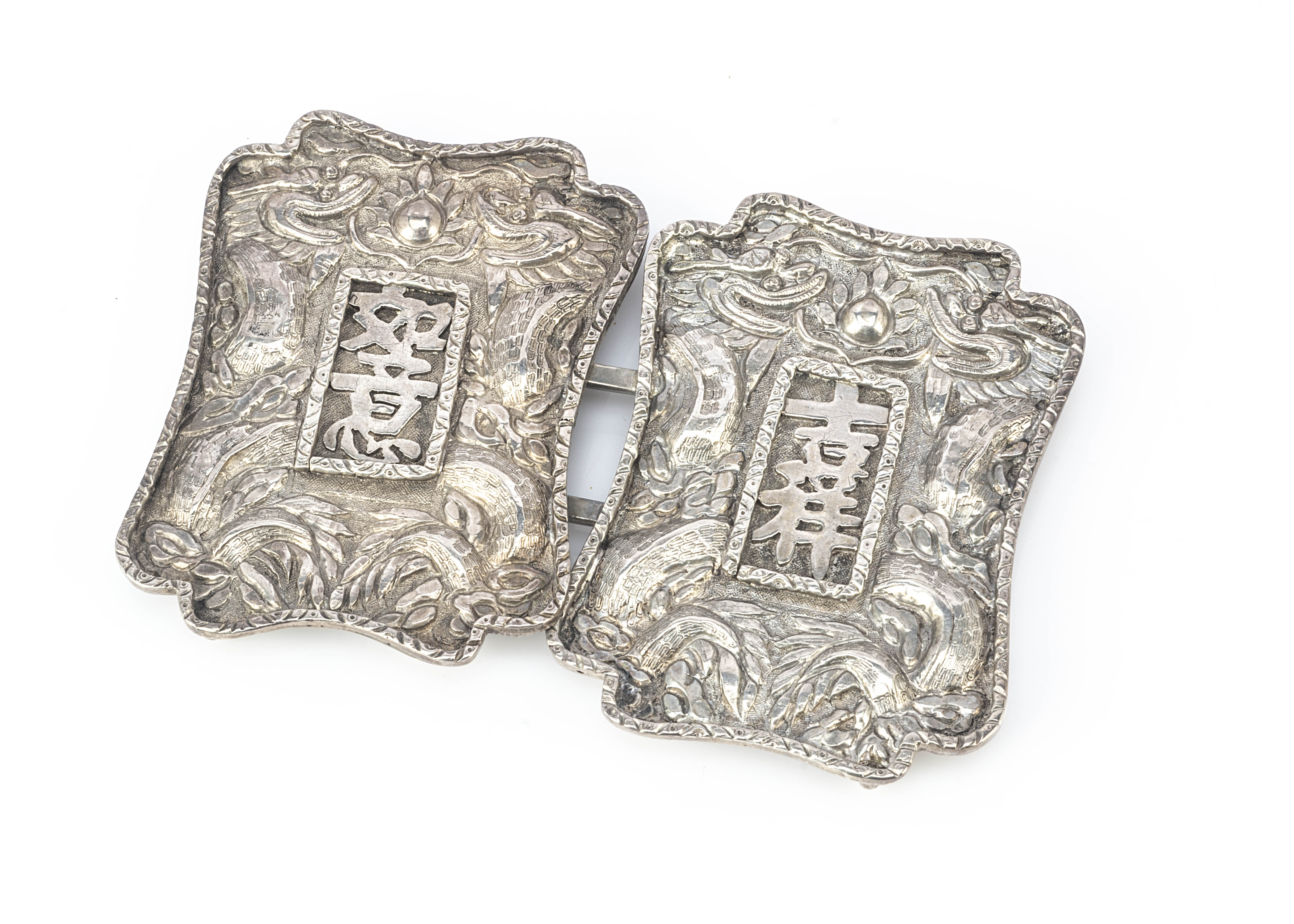 A white metal Chinese belt buckle, of shaped design centred with Chinese characters, 9.5cm x 6.