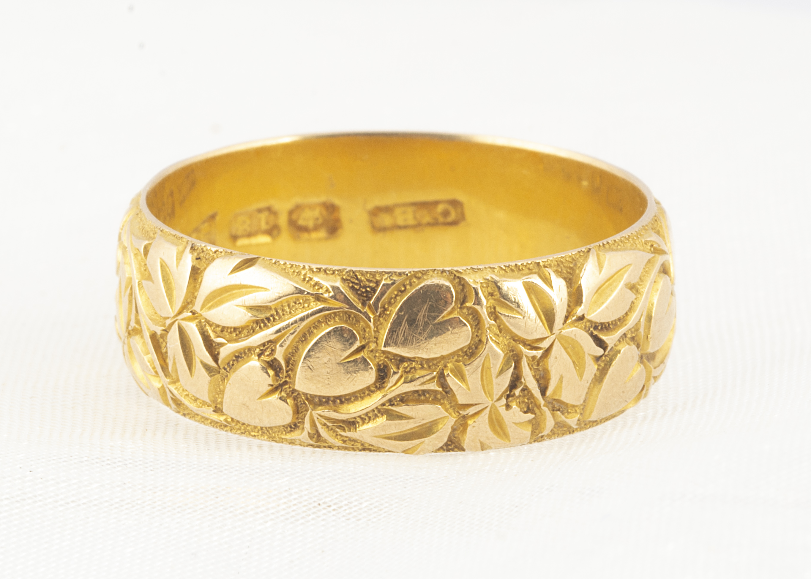 An 18ct gold engraved wedding band, of domed flattened form, with engraved hearts within a wreath of
