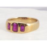 A three stone yellow metal ruby ring, the three step cut rubies in sunken settings, on a wide