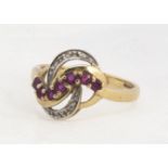 A 9ct gold ruby and diamond two colour crossover dress ring, the knot shaped top claw set with