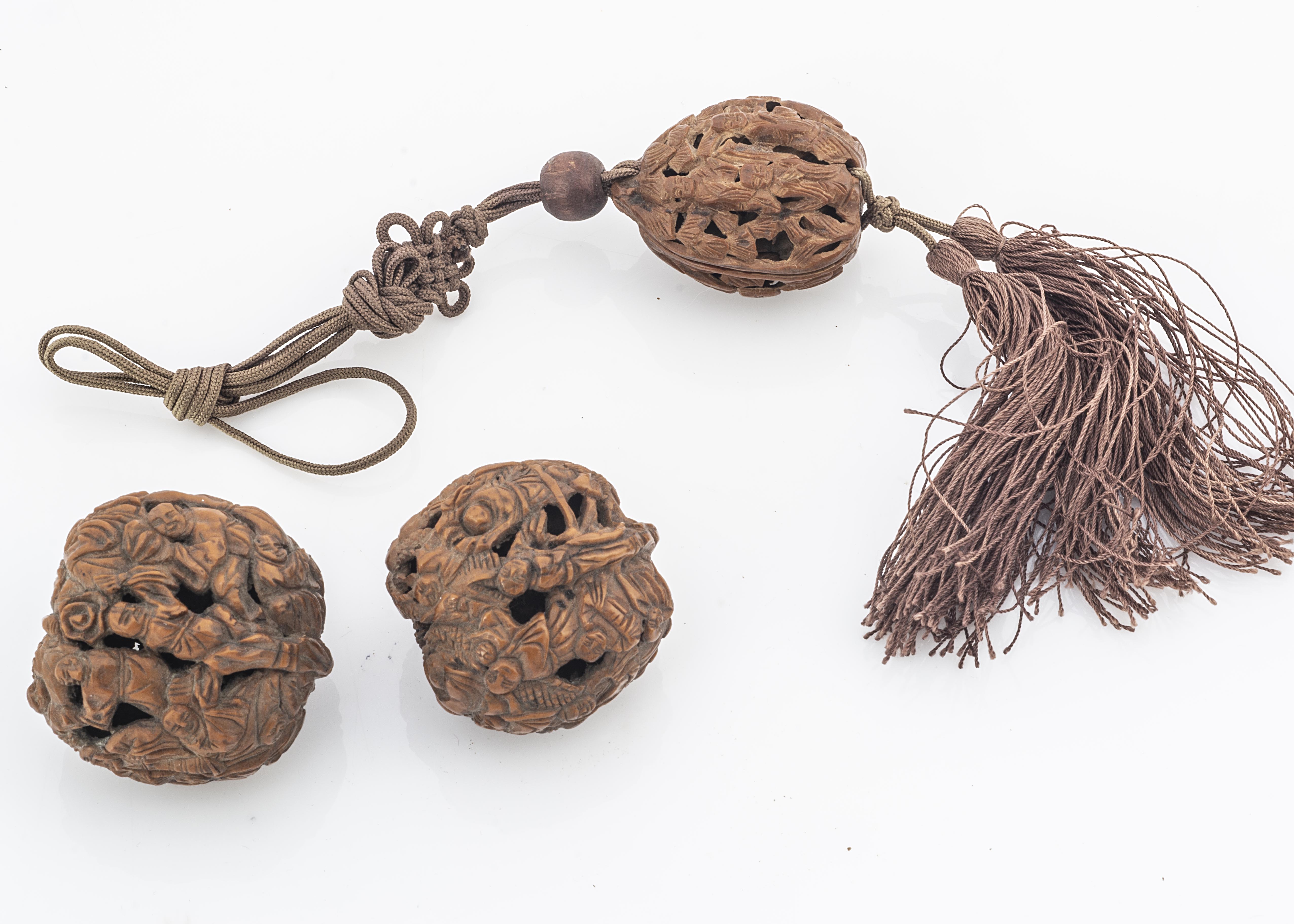 Three early 20th century Chinese carved walnut shells, the smallest with cord and tassels, each