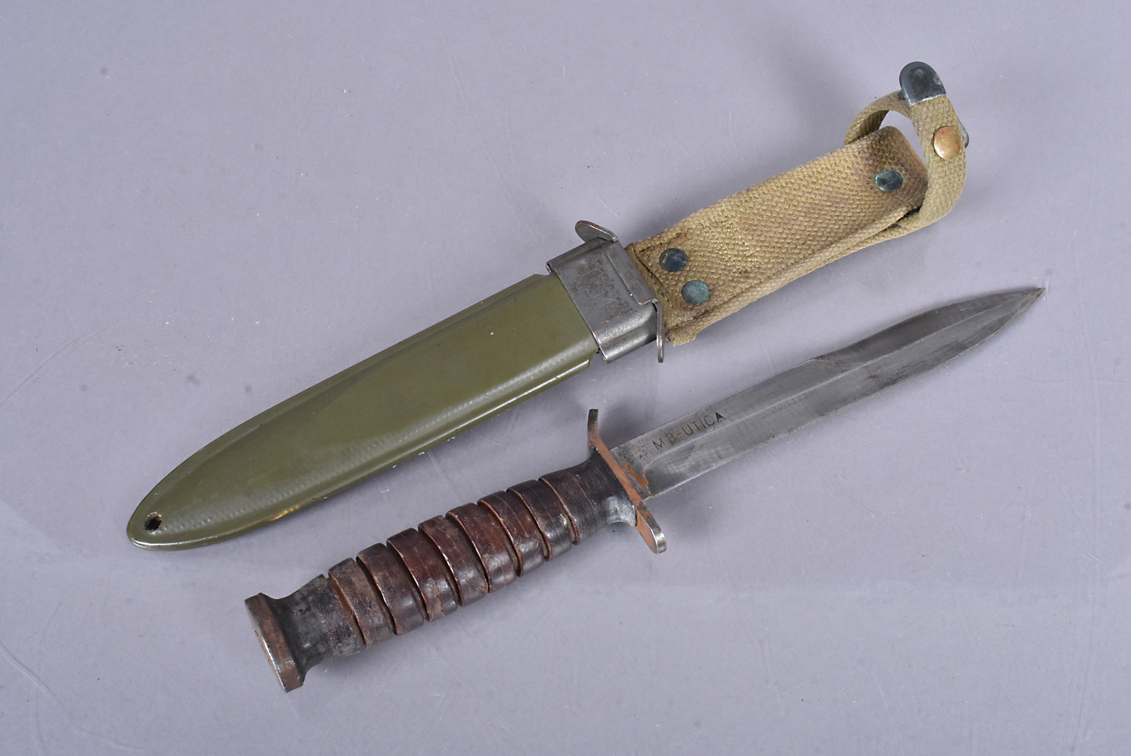 A WWII US M3 Combat Knife by Utica, marked to the blade, leather washer grip handle, oval metal