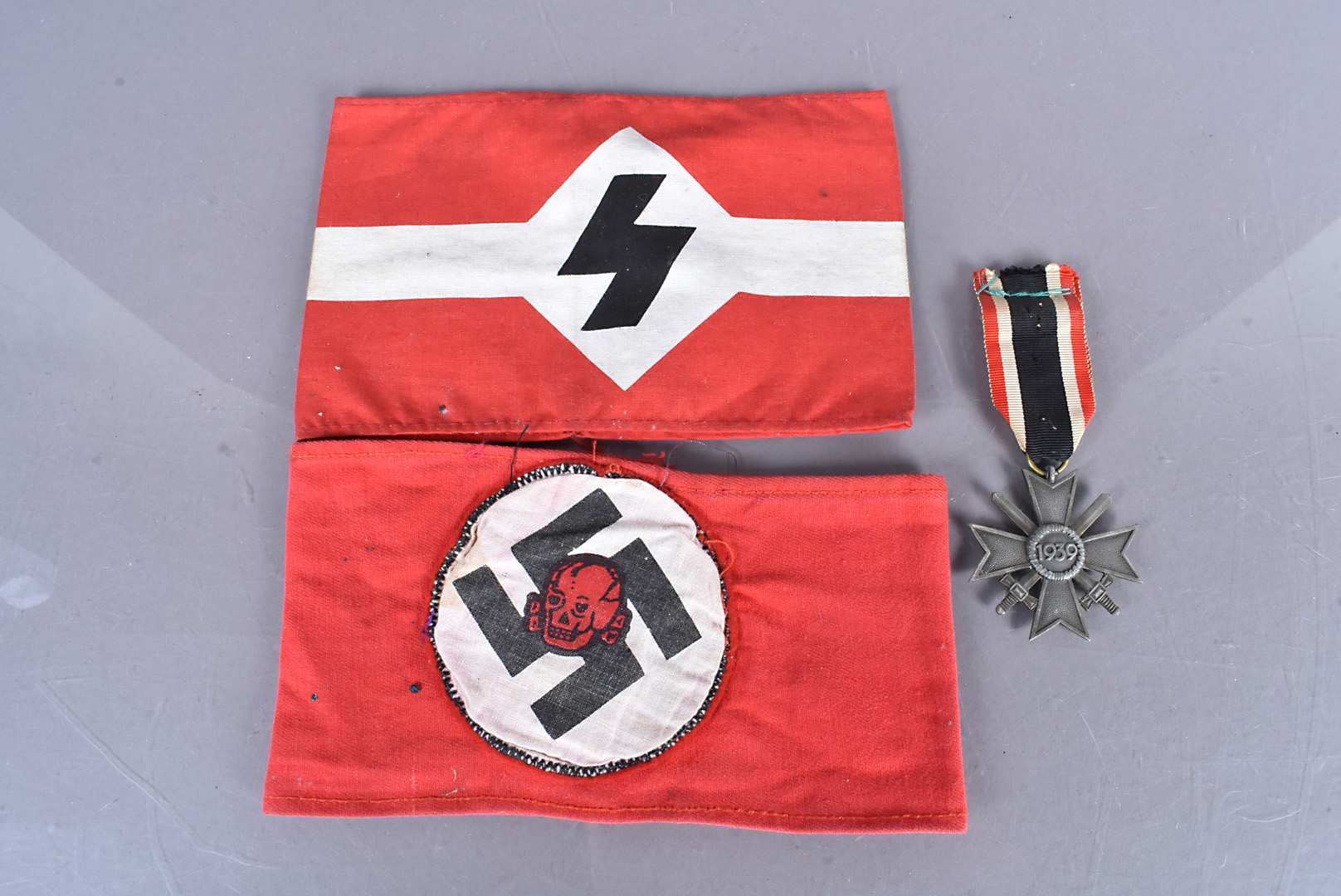 A WWII Merit Cross with Swords, together with two Third Reich Armbands (3) possibly reproduction,