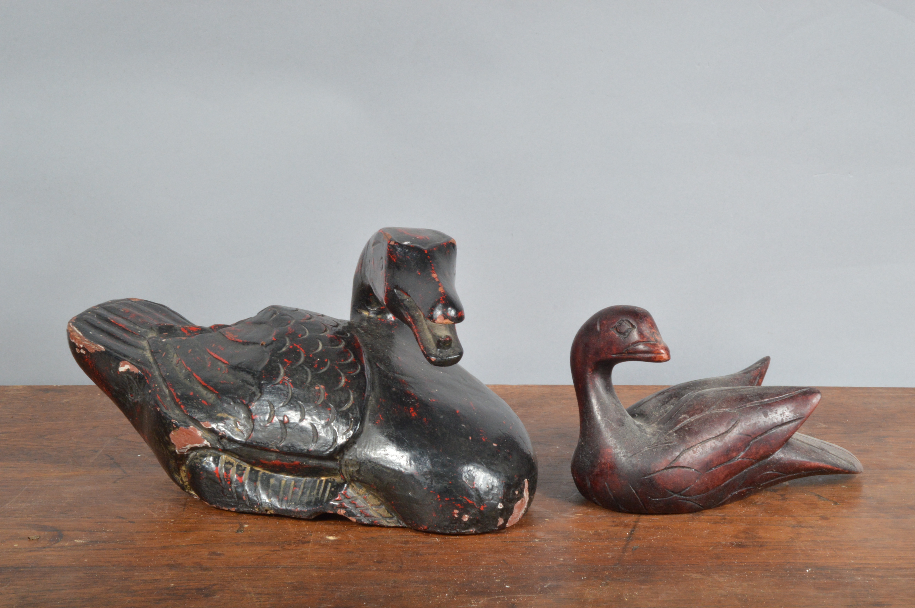 Two far eastern style decoy ducks, the largest example ebonised wood with a worn red painted finish,