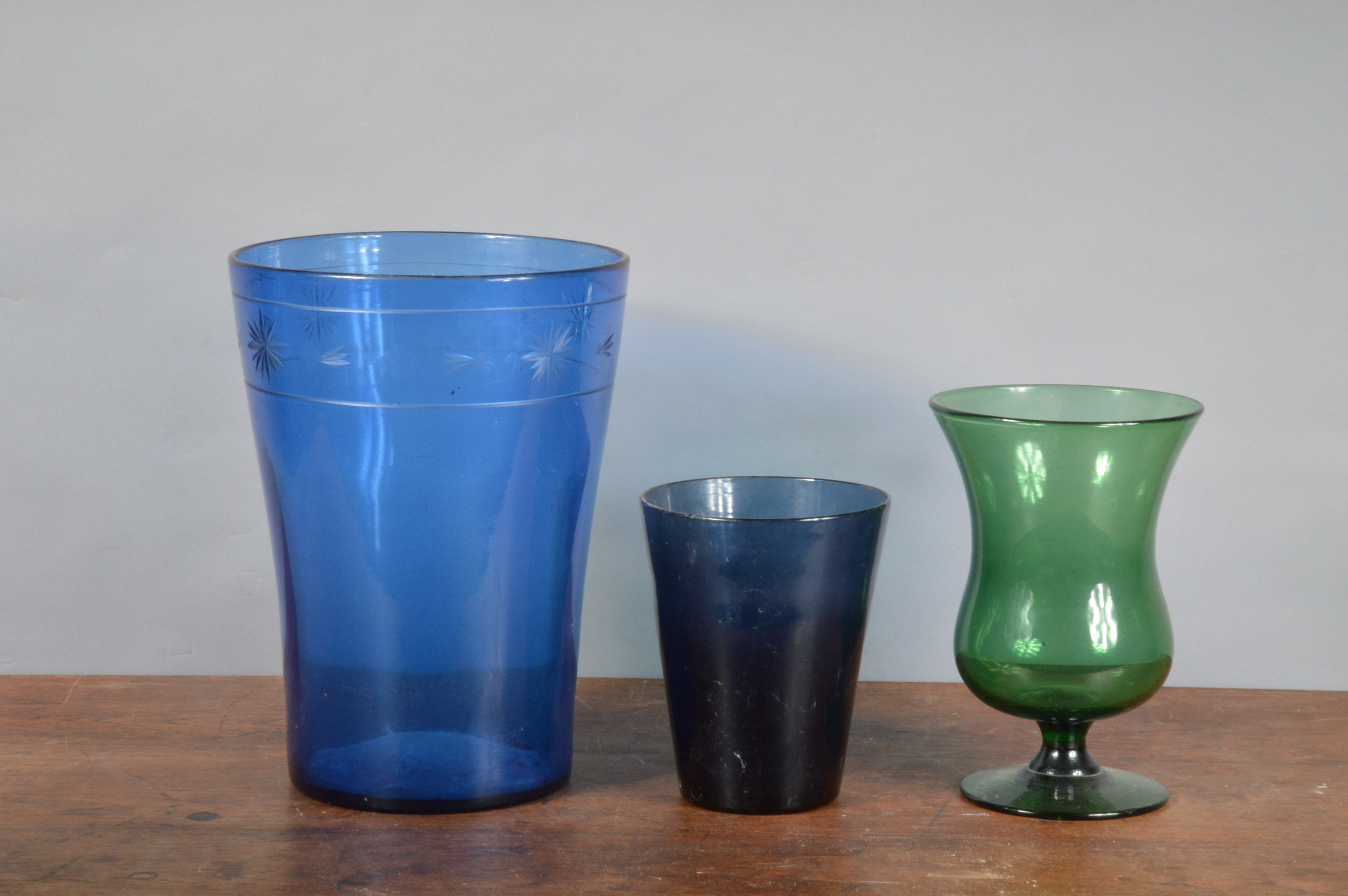 A large blue glass vase/waste paper bin, 33cm high, together with a green glass footed vase, 24cm