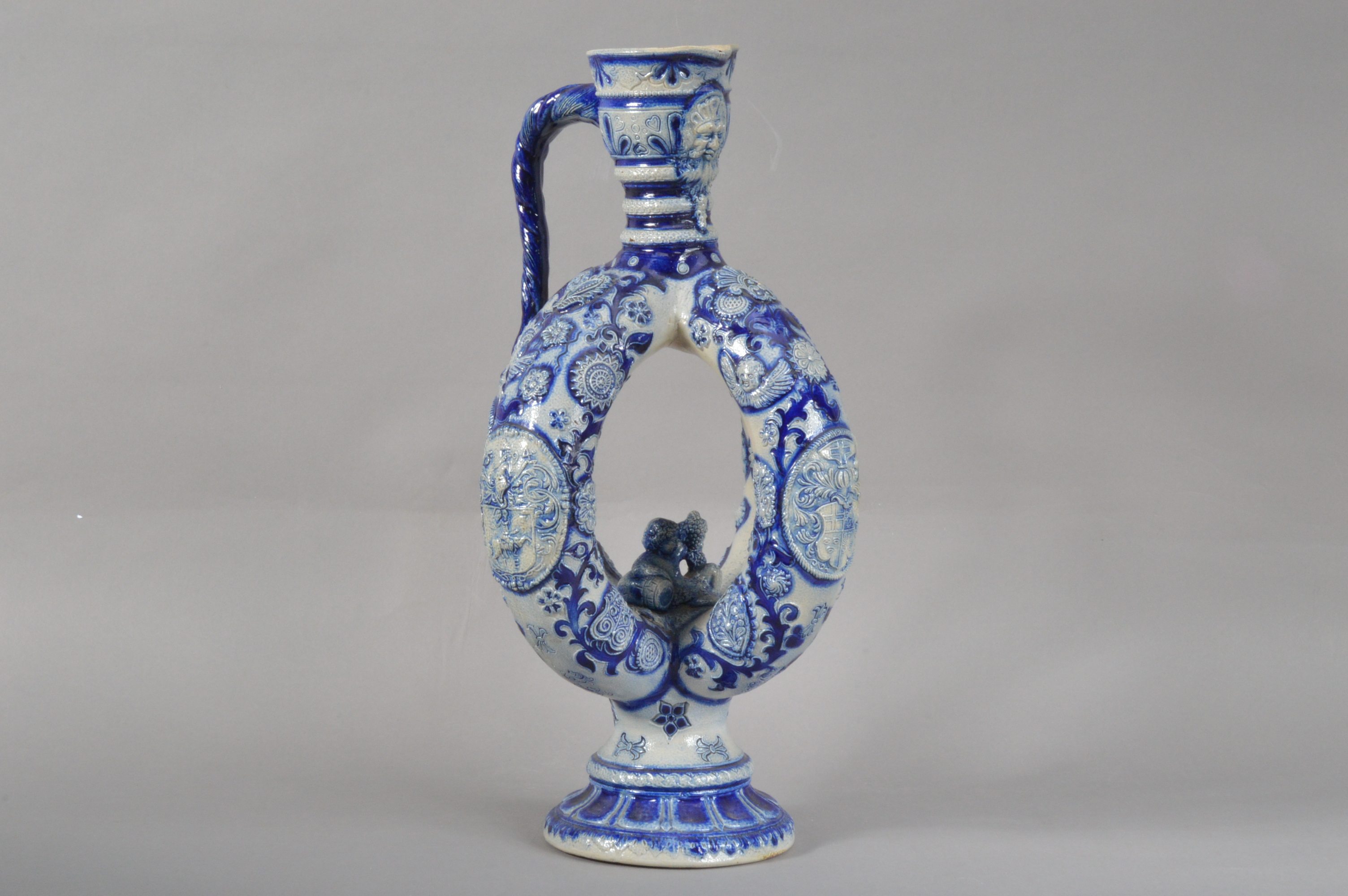 A German Westerwald salt-glazed stoneware ewer, blue and white raised decoration, a face below the