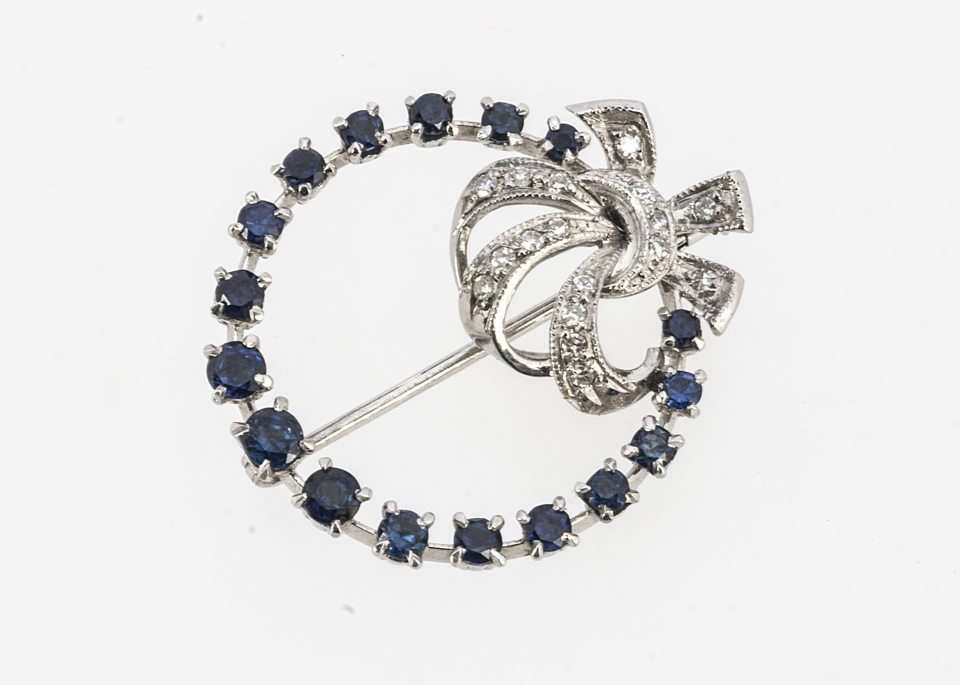 A continental white gold sapphire and diamond bow brooch, of open work circular design, round cuts