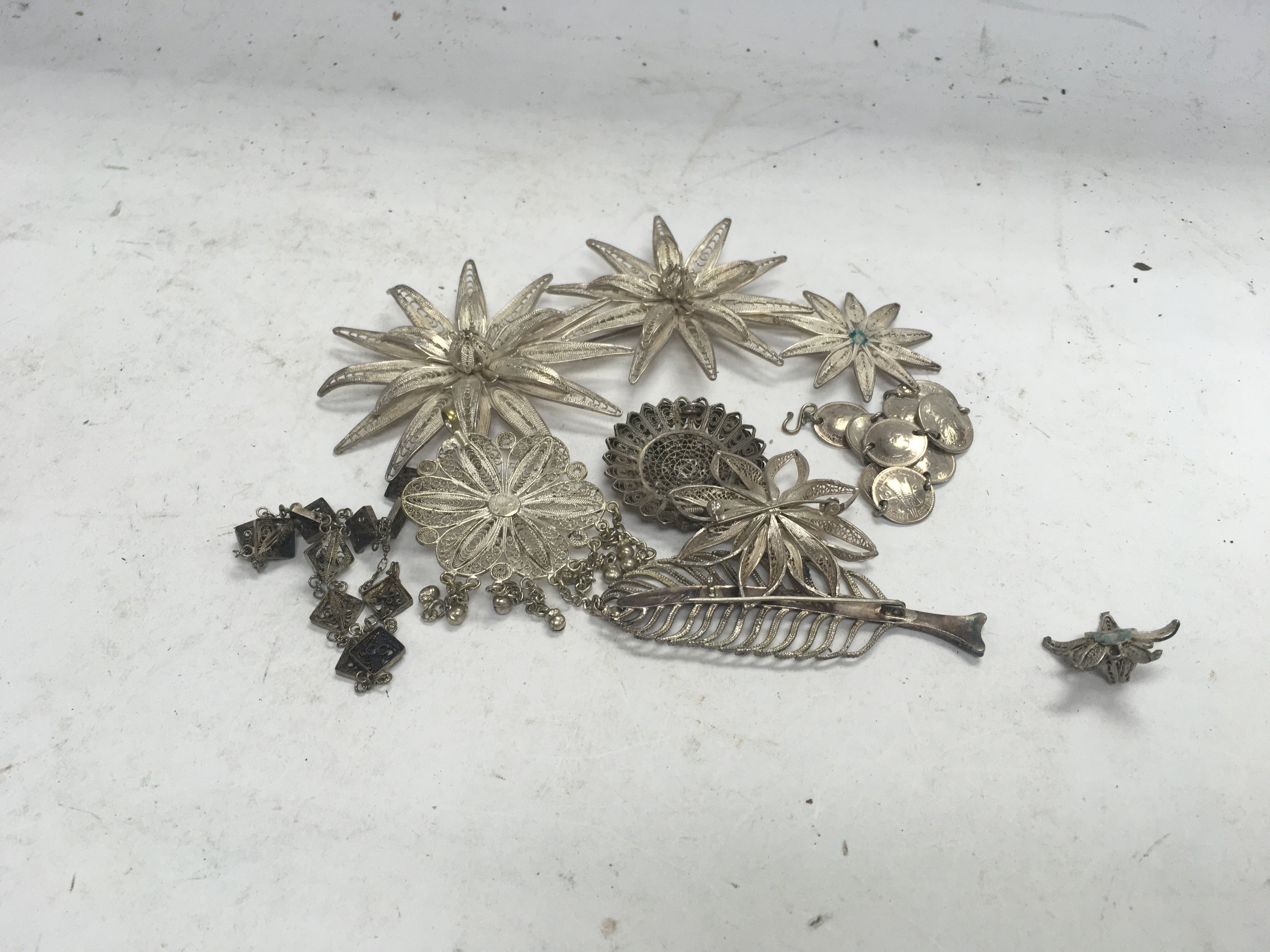 A collection of white metal Malaysian brooches a coin bracelet and other oddments