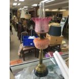 A Victorian brass oil lamp with a pink reservoir and a cranberry glass shade.