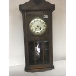 An oak wall clock with a a visible pendulum and si