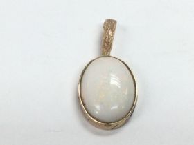 A yellow metal pendant set with an oval shaped whi