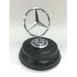 A Mercedes car badge raised on an ebonised base, approx height 14cm. Shipping category B.