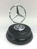 A Mercedes car badge raised on an ebonised base, approx height 14cm. Shipping category B.