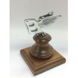 A Bentley car badge raised on a wooden plinth, approx height 13cm. Shipping category B.