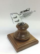 A Bentley car badge raised on a wooden plinth, approx height 13cm. Shipping category B.