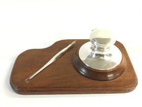 A silver hallmarked inkwell and dip pen on a wooden stand. Both engraved with initials MSV.