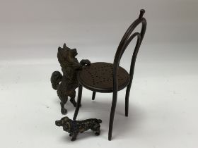 A small cast bronze dog figure leaning on a chair.