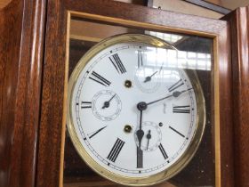A reproduction mahogany wall clock the circular dial with Roman numerals and visible pendulum