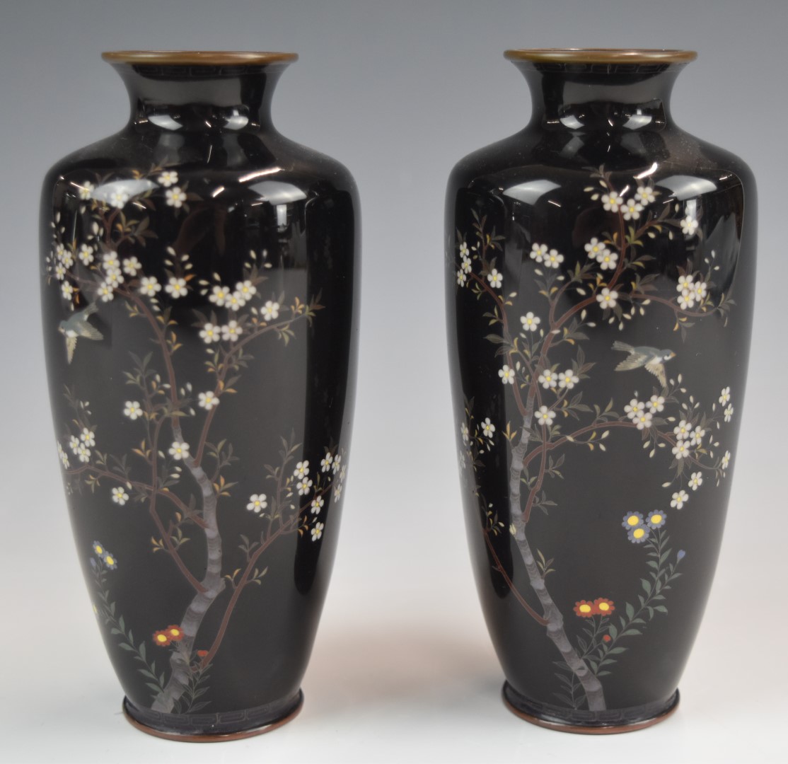 A pair of Japanese cloisonné vases decorated in enamel with birds, trees and flowers on a dark