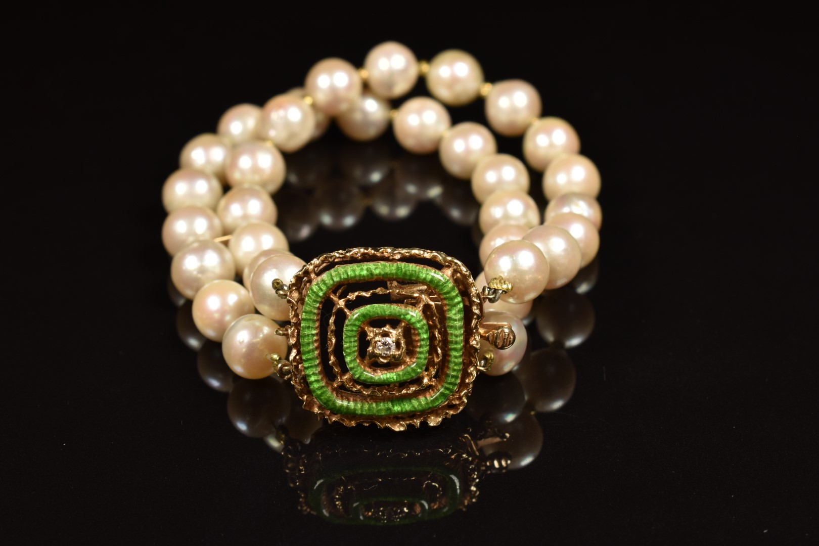 A double strand cultured pearl bracelet, the 14k gold clasp set with a diamond and green enamel