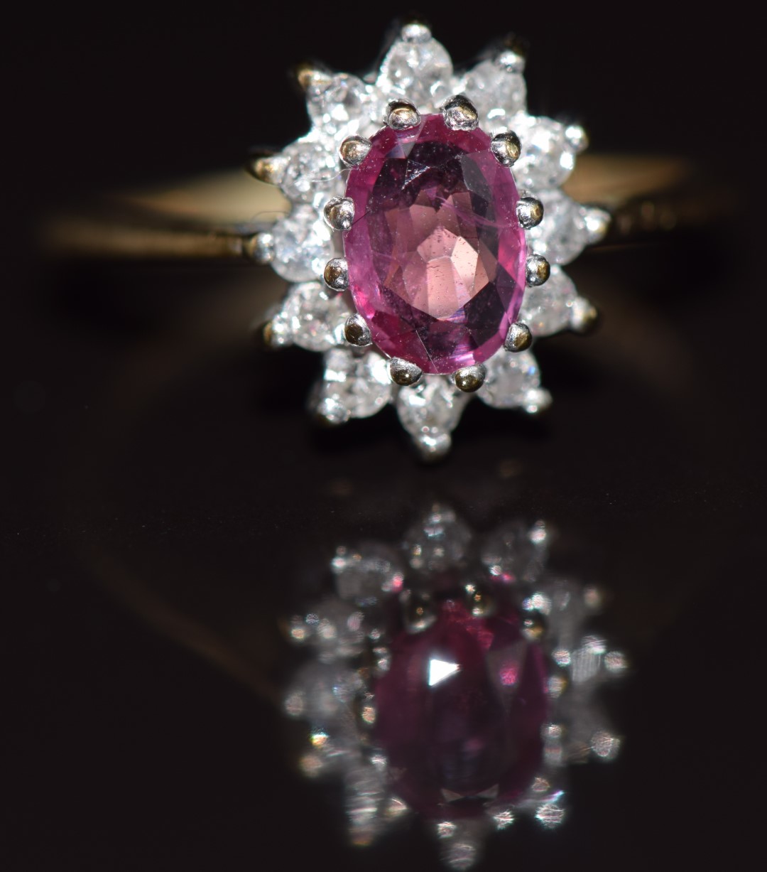 A 9ct gold ring set with an oval cut pink sapphire surrounded by diamonds, 1.7g, size E