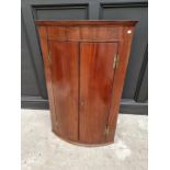 A George III mahogany and line inlaid bowfront hanging corner cupboard, 110cm high x 71cm wide.