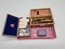 A small lacquered brass field microscope, in fitted box; together with a small quantity of slides