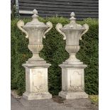 A pair of large carved limestone lidded urns with handles on pedestals