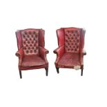 A PAIR OF GEORGIAN DESIGN WING ARMCHAIRS In red leather button back upholstery on mahogany legs. (