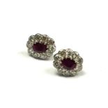 A PAIR OF PLATINUM, RUBY AND DIAMOND CLUSTER EARRINGS The oval cut ruby edged with round cut