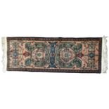 A PERSIAN WOOLLEN RUNNER RUG Having scrolled green motifs to central field on pink ground with
