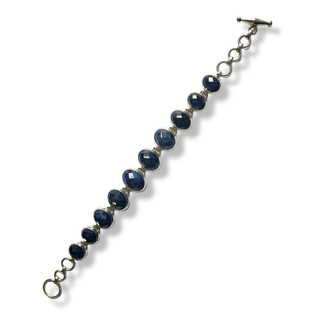 A WHITE METAL AND SAPPHIRE BRACELET Having row of graduated faceted oval cut sapphires. (central