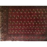 A BOKHARA WOOLLEN RUG Having five rows of gul motifs to central field on a red ground contained