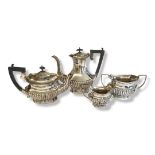 AN EARLY 20TH CENTURY FOUR PIECE SILVER TEA SET Having a carved ebonised wooden handle and fluted